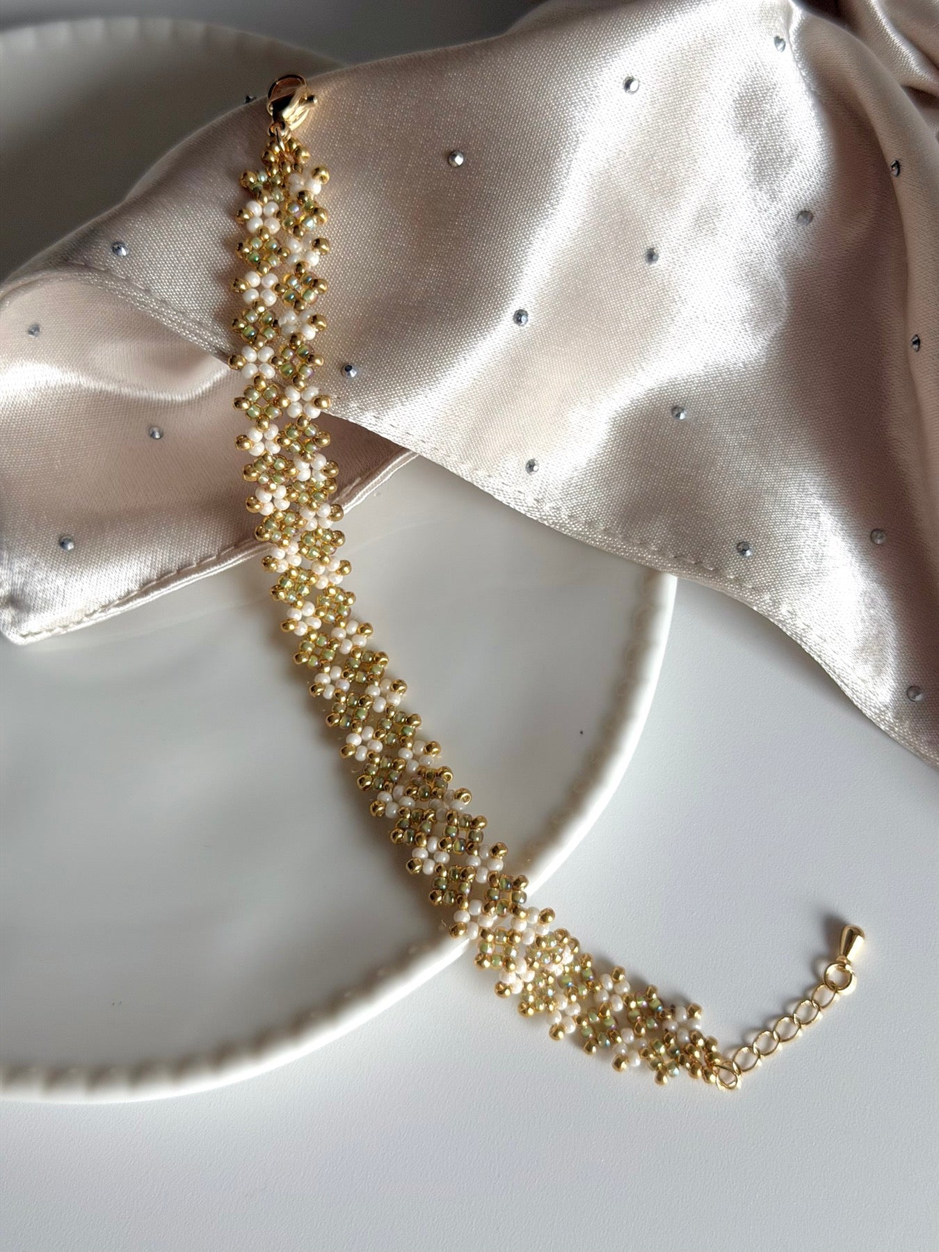Ivory and gold-toned seed bead bracelet laid on pale satin fabric